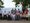 Eine große Gruppe von Menschen posiert lächelnd für ein Gruppenfoto im Freien. Viele tragen blaue Baseballkappen. Zwei Personen sitzen in Rollstühlen. Im Hintergrund erstreckt sich eine weite Landschaft mit Feldern, gerahmt von grünen Bäumen.