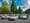 Eine Gruppe von Menschen posiert lächelnd neben mehreren weißen Autos auf einem Parkplatz. Im Hintergrund stehen hohe Bäume und ein großes Gebäude unter einem blauen Himmel mit weißen Wolken.
