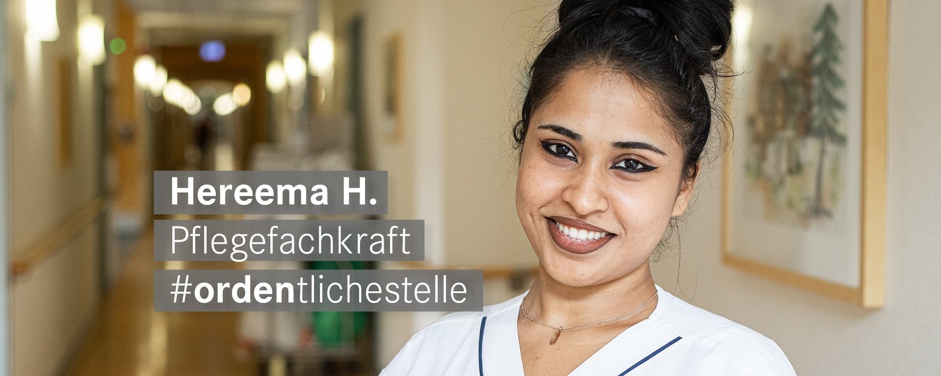 Pflegekraft mit schwarzen Haaren und Dutt laechelt freundlich in die Kamera