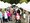 Ein belebter Außenmarkt mit Reihen weißer Zelte. Menschen gehen auf einem gepflasterten Weg entlang. Im Vordergrund sitzt ein älterer Mann in einem Rollstuhl. Rechts sind Gemälde ausgestellt.